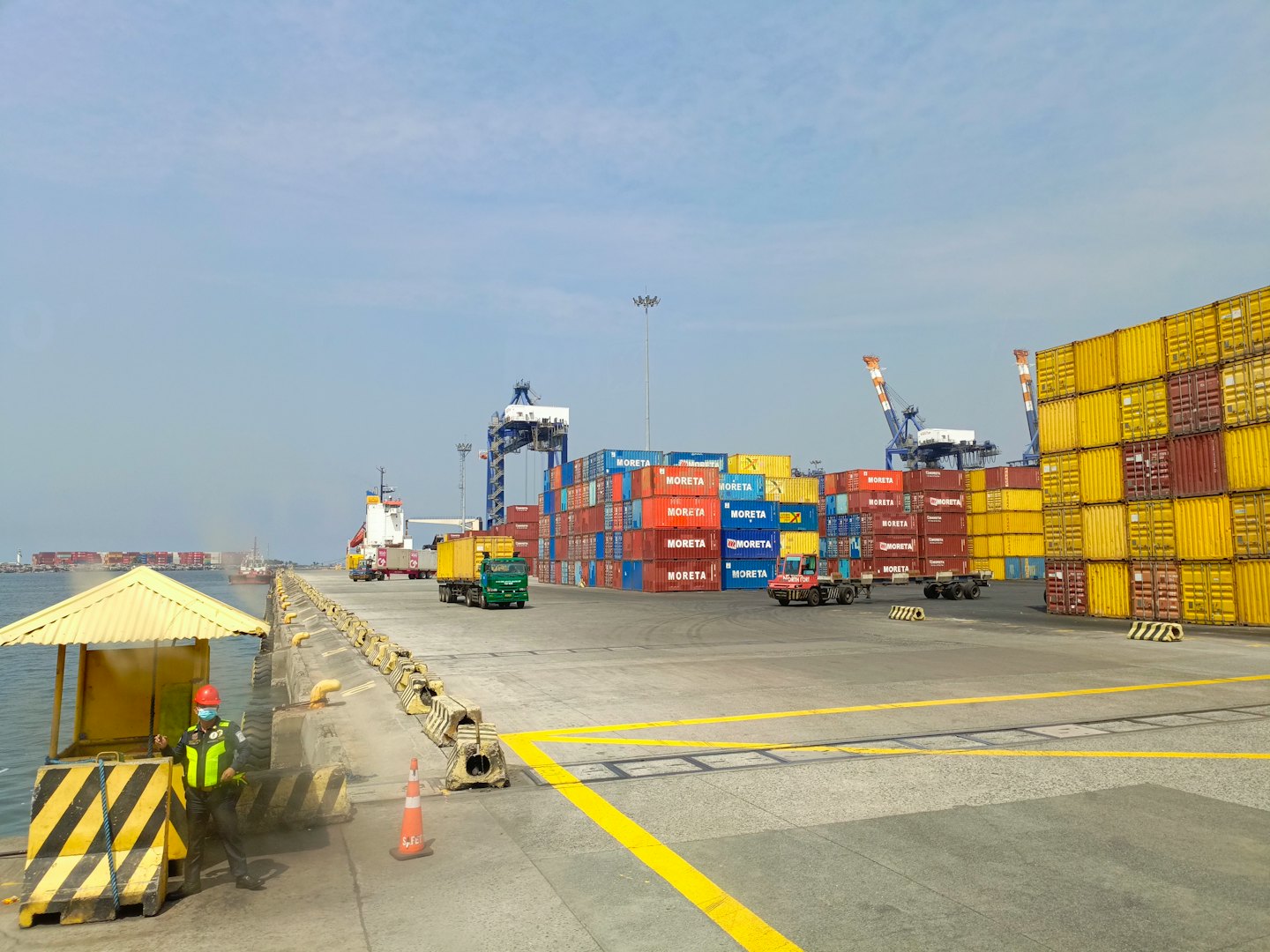 Un operaio con giubbotto di sicurezza si trova in un porto commerciale affollato.
