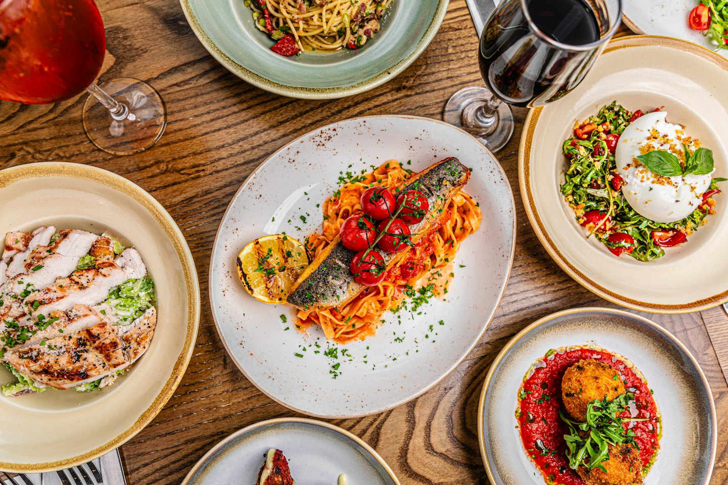 Piatti gourmet e bicchieri di vino disposti su un tavolo di legno.